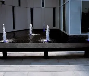 Modern Langley concrete bench in front of a water fountain with LED lighting near commercial building