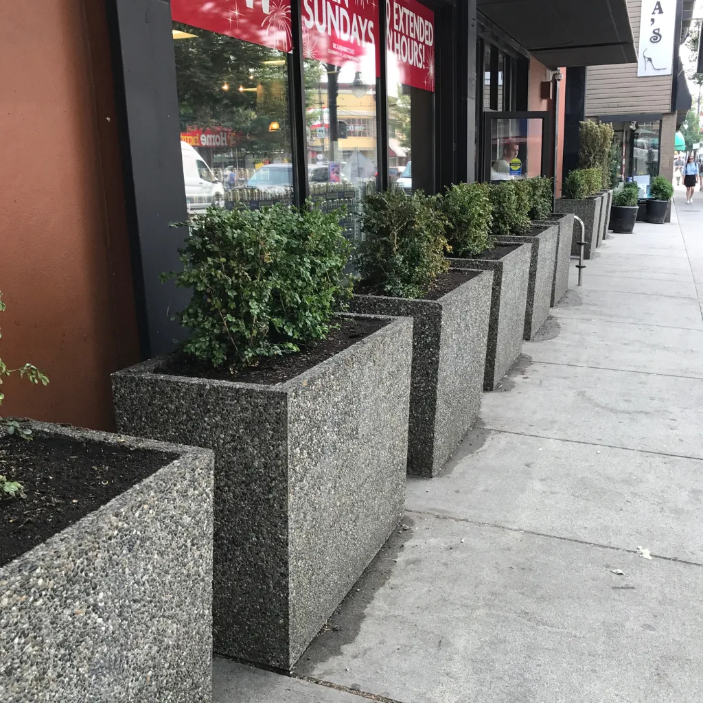 Outdoor concrete planters lining a storefront sidewalk in exposed aggregate finish